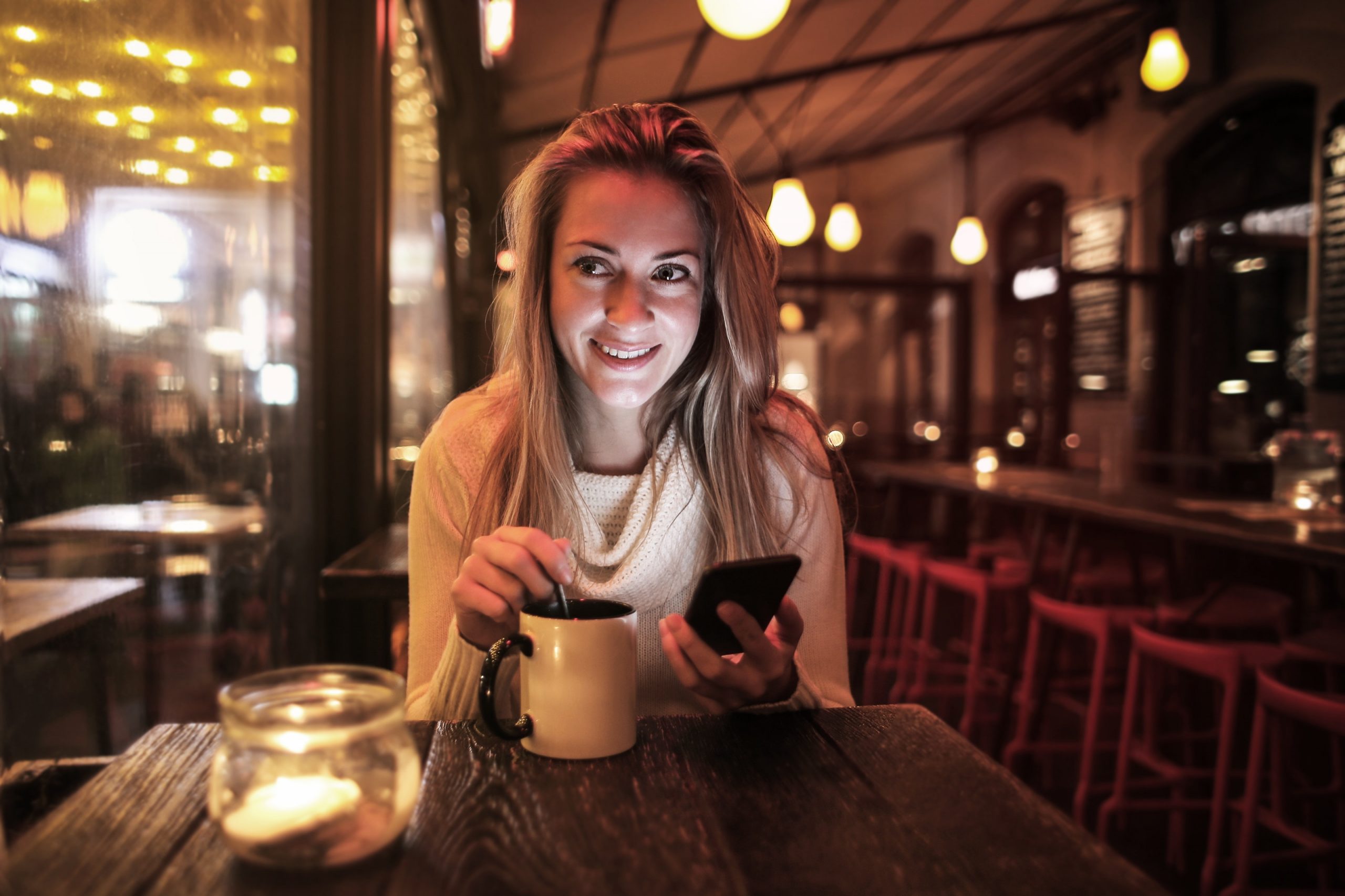 woman drinking tea, using phone, and smiling at a table by herself