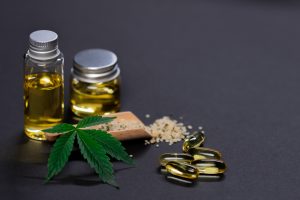 CBD oil capsules and marijuana leaves on gray background