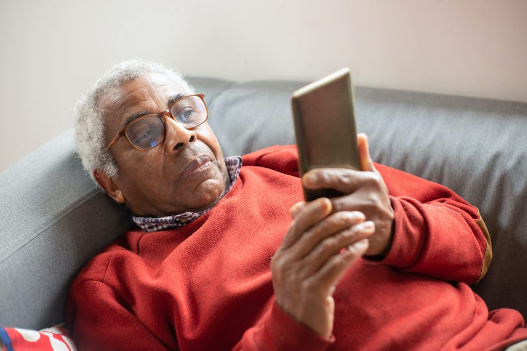 older man lying on couch using his phone