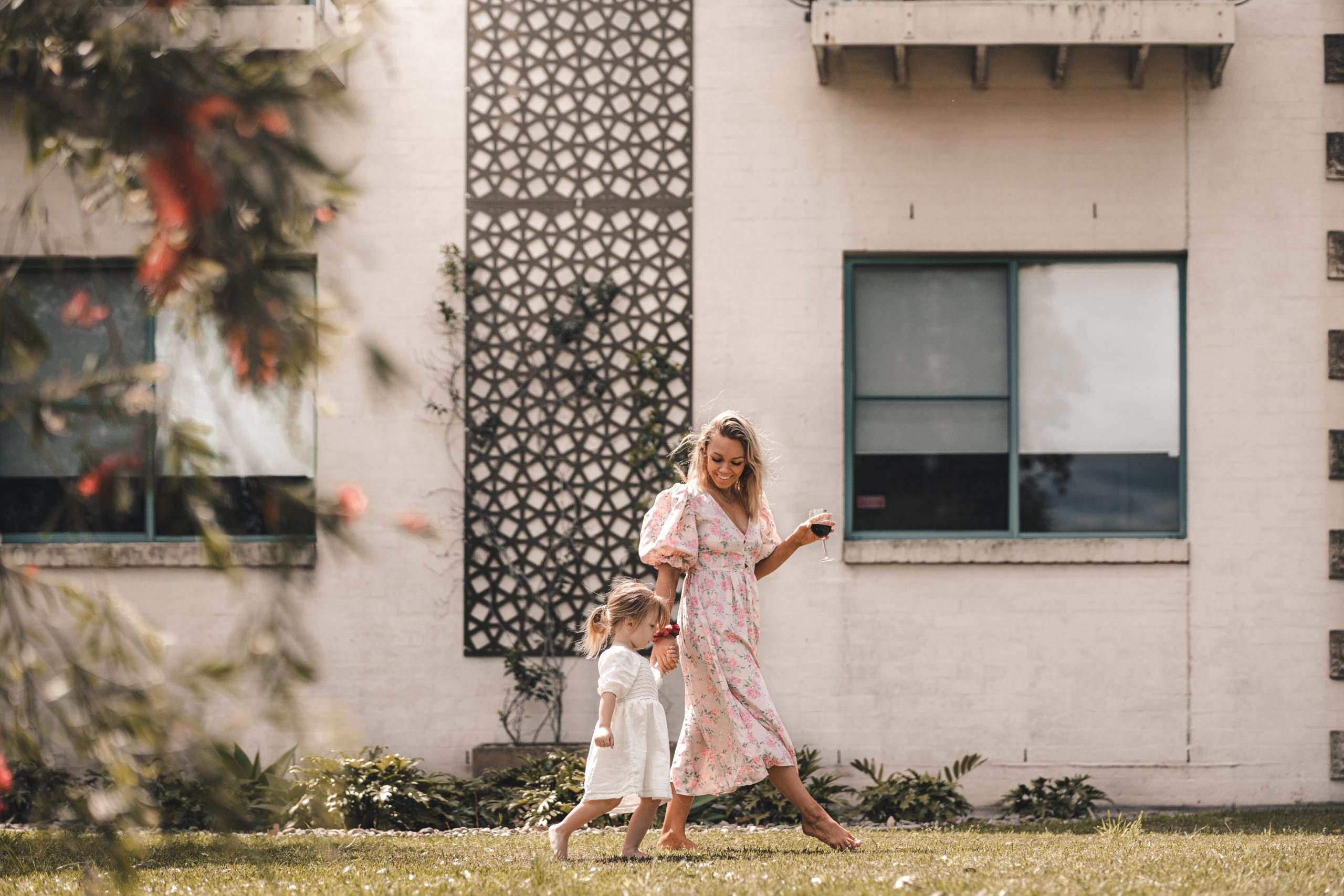 mother holding wine glass while walking on lawn with daughter