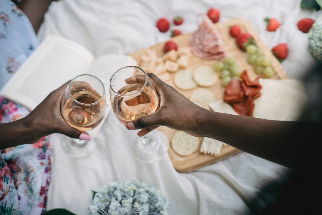 two hands clinking white wine glasses over appetizers