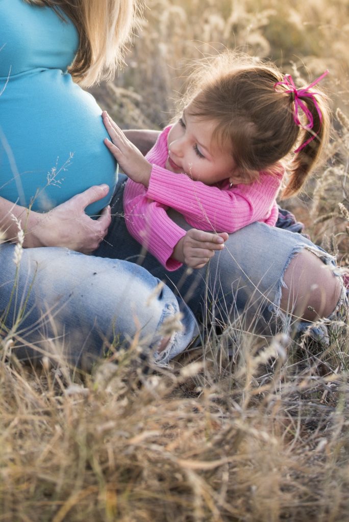 child touching mother's belly while sitting on grass