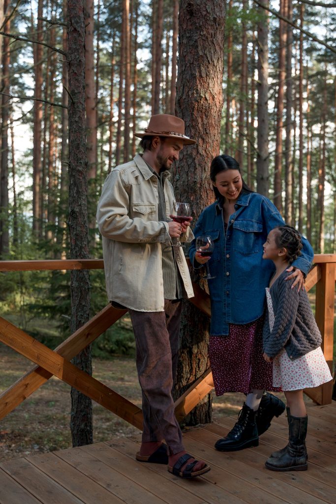 mother and father standing on bridge with wine glasses and child