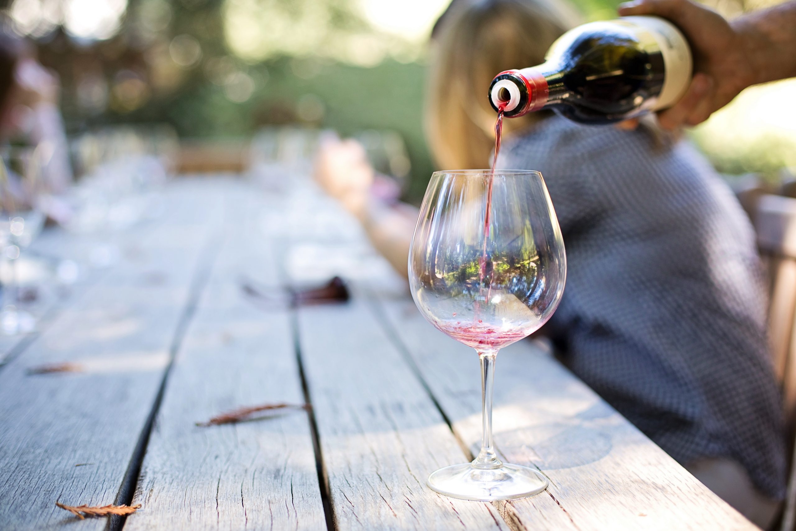 person pouring wine into glass at outdoor table