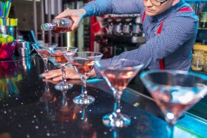 bartender in suspenders preparing a line of cocktails