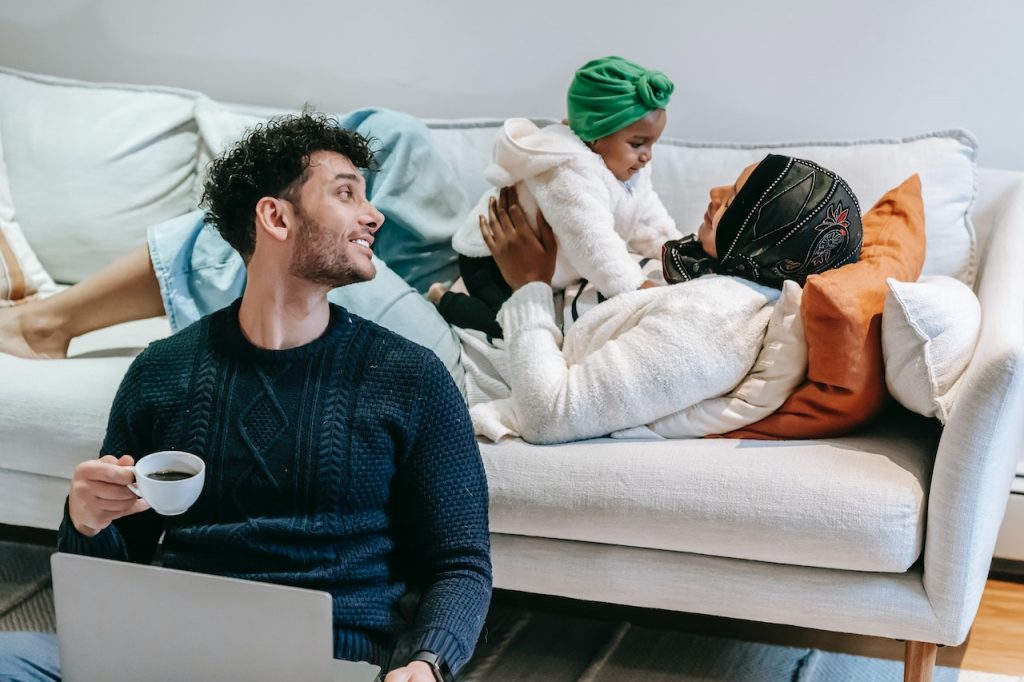 young man drinking coffee by couch with wife and child