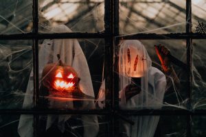 two people in ghost costumes holding jack o lanterns in a window