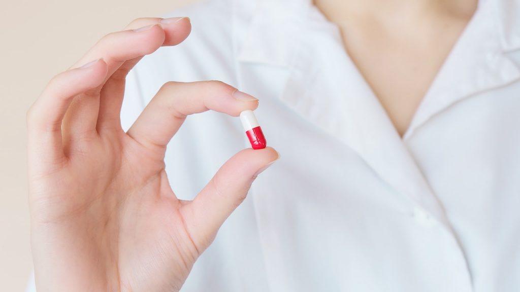 doctors hand holding red and white pill