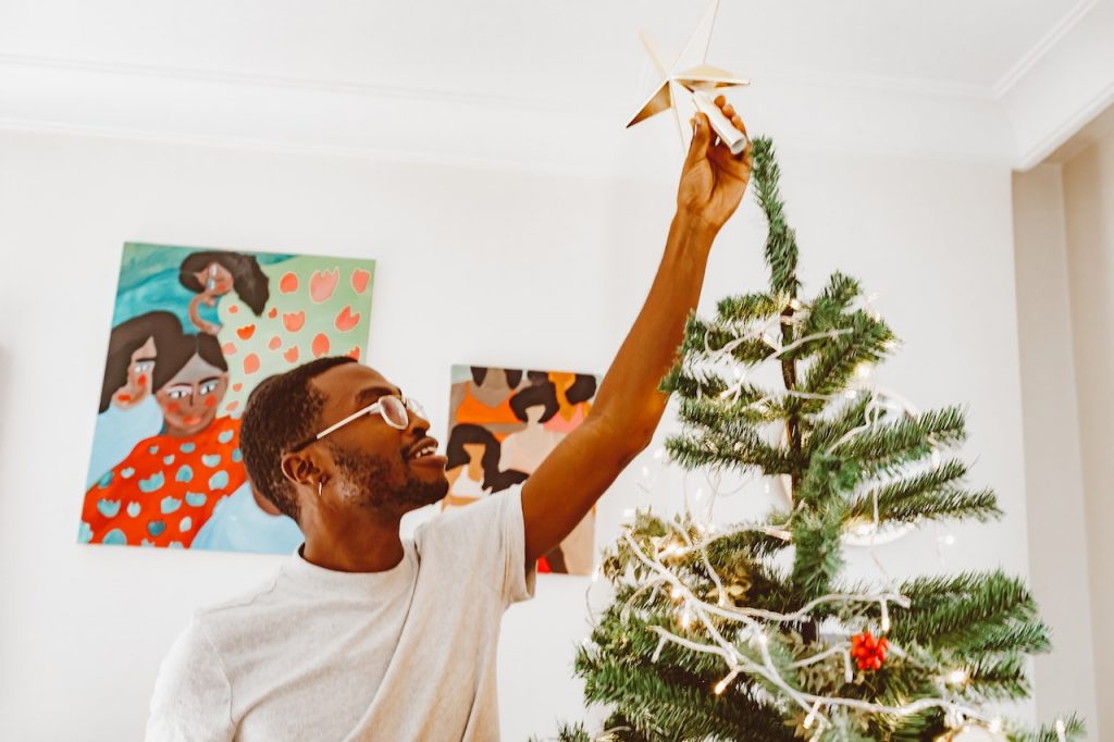 man hanging christmas ornament on tree