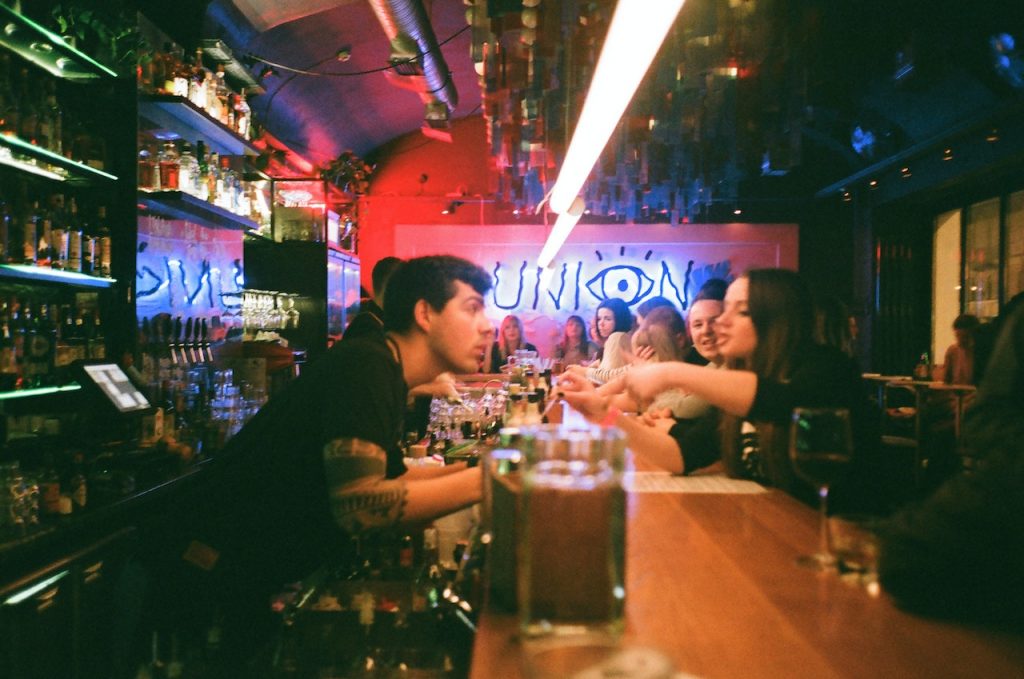 bartender leaning over busy bar to talk to customer