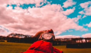 Hand with wristwatch against pink clouds