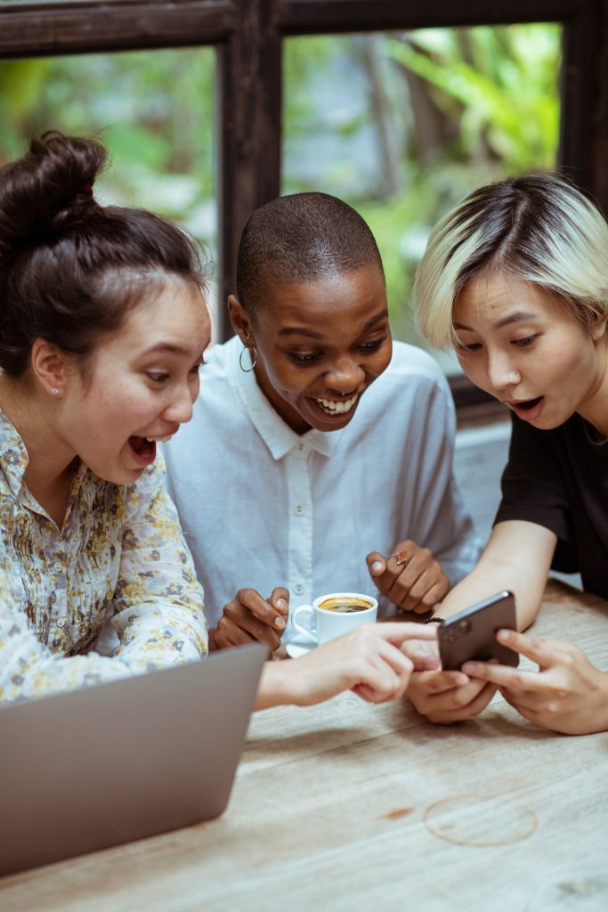 delighted female friends gathered around smartphone
