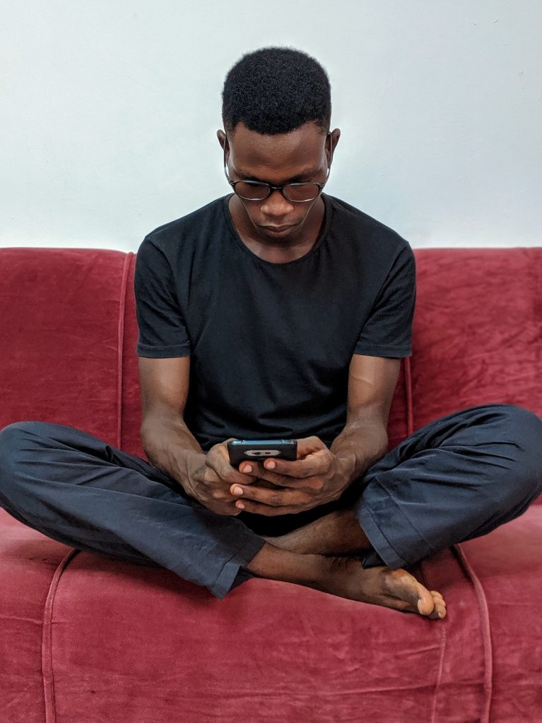 young man sitting on red couch looking at smartphone