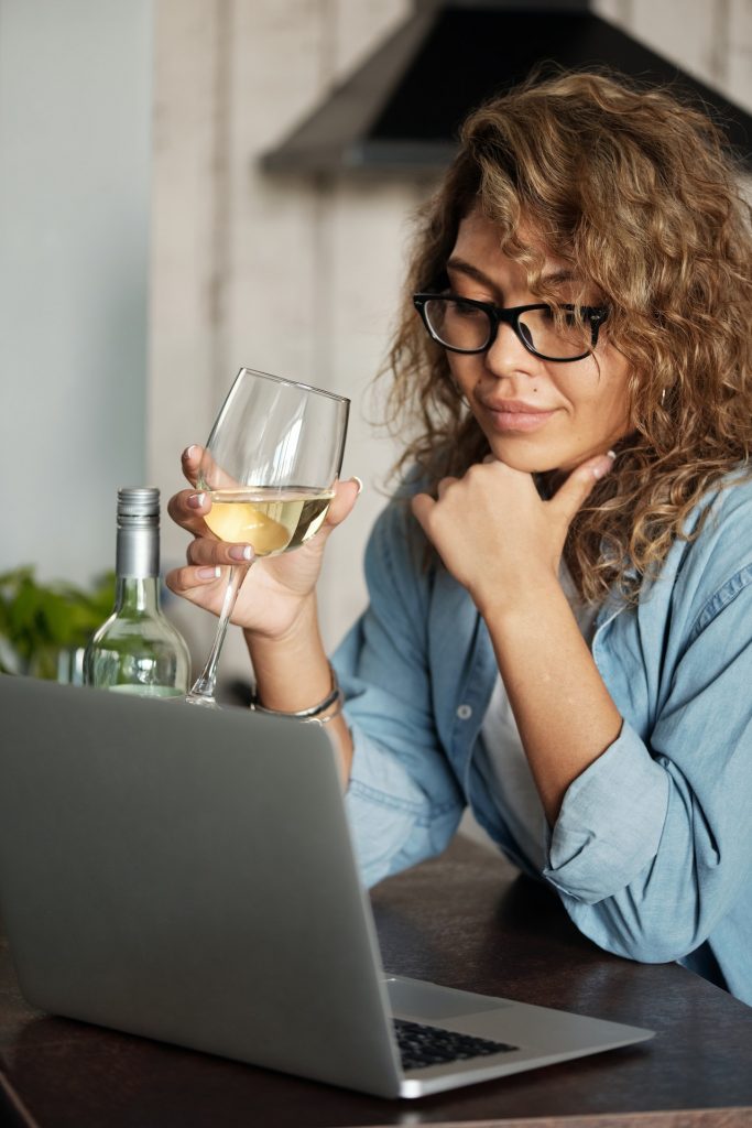 woman holding glass of wine in front of laptop