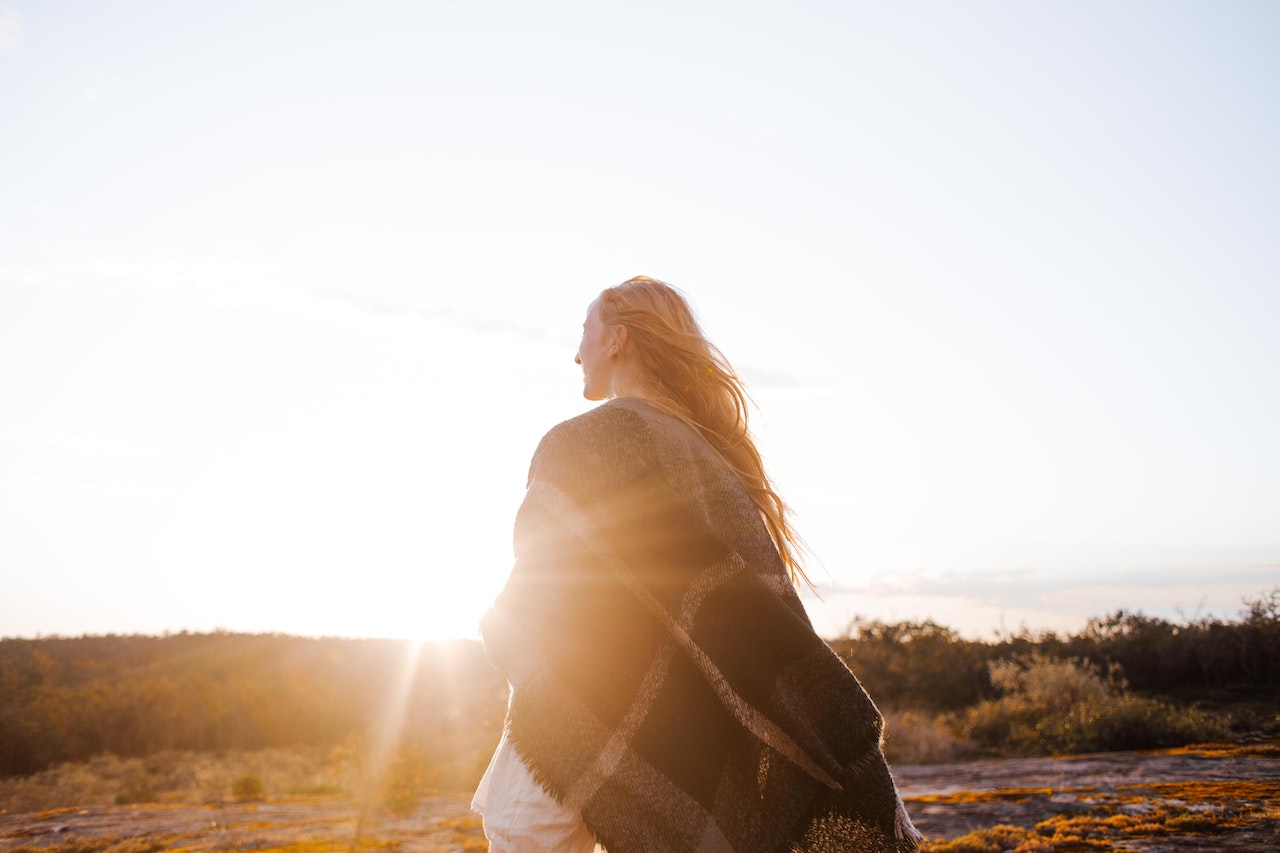 woman facing sunrise wrapped in plaid blanket