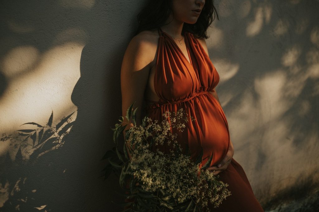 pregnant woman in orange dress leaning against wall