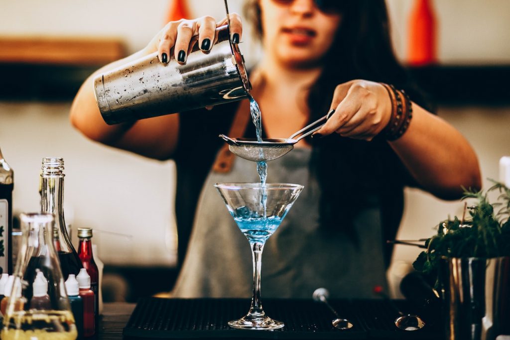 female bartender pouring blue cocktail into martini glass