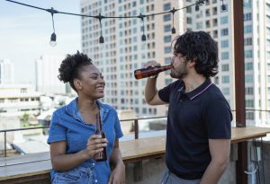 man and woman drinking beer and flirting on rooftop bar