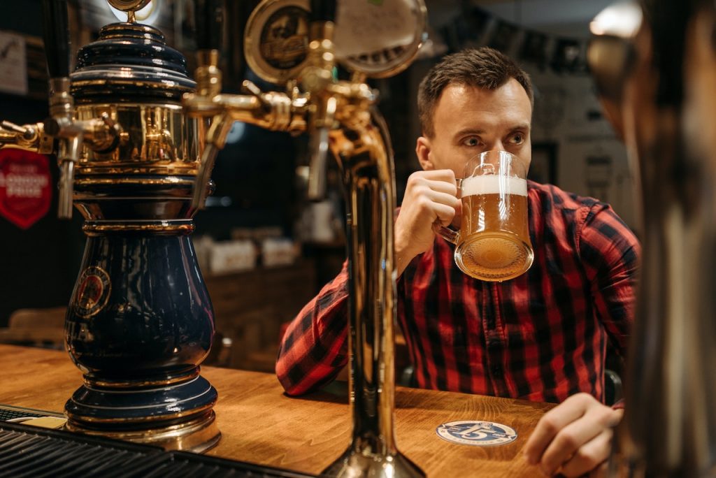 man in red plaid shirt drinking a draft beer at a bar