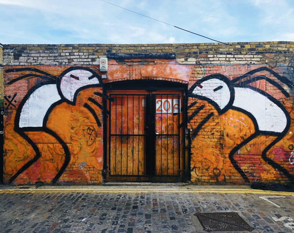 orange and white street art of two figures vomiting by a stone gate