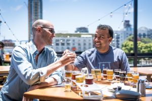 two men clinking beer glasses at a rooftop bar