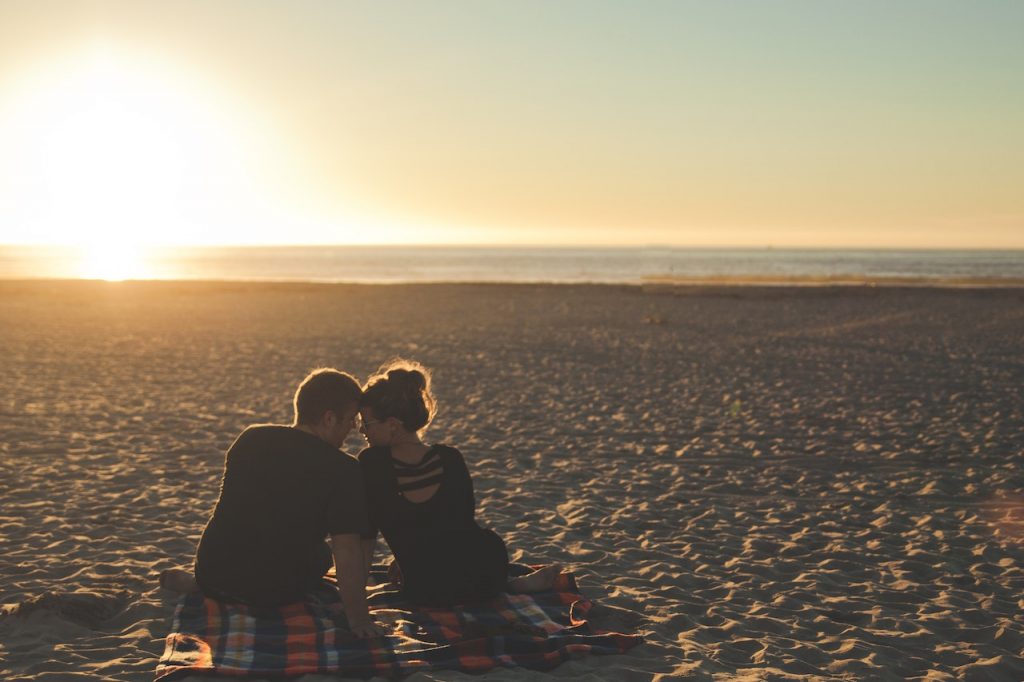 man and woman cuddling on beach blanket romantic evening