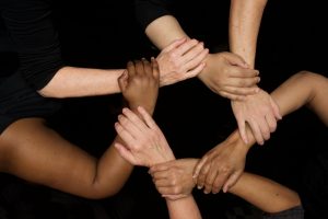 Several people's hands are joined by holding each other's wrists, to form a circle as a symbol of unity and community.