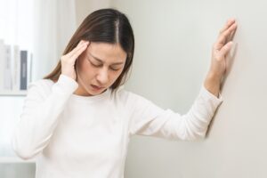 Woman leans against wall and holds her head with her other hand.